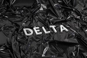 la palabra delta colocada con letras de metal plateado sobre fondo de bolsa de plástico negro arrugado en perspectiva diagonal foto