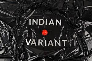 words indian variant laid with silver metal letters on crumpled black plastic bag background with small virus model photo