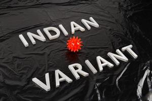 words indian variant laid with silver metal letters on crumpled black plastic bag background with small virus model photo