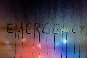 the word emergency written on night wet window glass close-up with blurred background photo