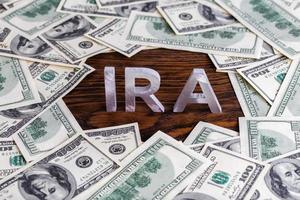 the word ira made of silver metal letters on wooden background surrounded by us dollar banknotes photo