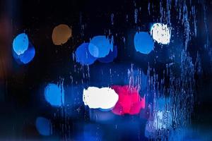 an abstract background of red and blue police lights bokeh trough wet glass at night close-up with selective focus photo