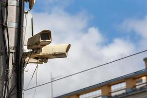 two old cctv security surveillance cameras on street light pole on blue sky background photo