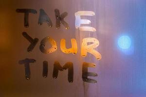 the phrase take your time written by finger on night wet glass with blurred street lights, close-up with selective focus photo