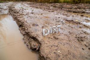 the word dirt composed of silver metal letters on wet clay surface photo