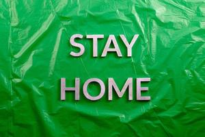 the words stay home laid with silver metal letters on crumpled green plastic background in flat lay perspective photo