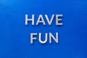 the words have fun laid with silver metal characters on blue painted wooden board in central flat lay composition photo