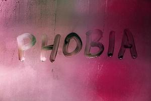 the word phobia handwritten on wet foggy window glass surface with red background light photo