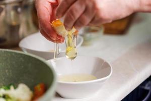 senior caucasian woman hands breaking white chicken egg above white bowl photo