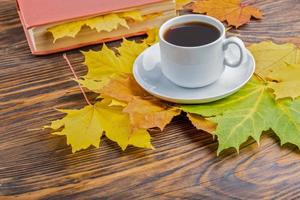 taza de café sobre una mesa de madera con un libro y coloridas hojas de arce otoñales foto