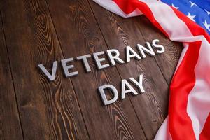 the words veterans day laid with silver metal letters on wooden board surface with crumpled usa flag at right side with diagonal perspective photo