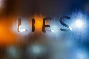 the word lies written on night wet window glass close-up with bokeh background photo