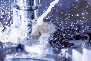 Close-up view of vertical cnc steel milling process with external water coolant streams, splashes and a lot of metal chips, high contrast photo