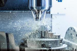 Vertical photo of industrial wet milling process in 5-axis cnc machine with coolant flow under pressure and freezed splashes