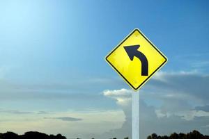 Traffic warning sign on pole, left curve means the way ahead is a right curve and should slow driving and drive carefully. photo