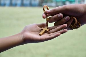 Closeup hands which offering wooden cross bead rosary to other people concept, soft and selective focus.