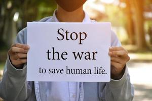 Asian boy shows white paper which has text Stop the war to save human life. Soft and selective focus, concept for calling all people to stop the war around the world. photo