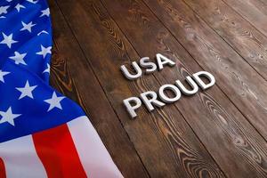 words USA proud laid with silver metal letters on brown wooden surface with flag of United States of America photo