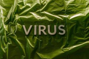 the word virus laid with silver metal letters on green crumpled plastic film with dramatic light photo