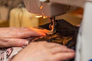 una vista de cerca del proceso de costura, la mano de una anciana usando una máquina de coser, técnica de enfoque selectivo foto