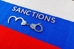 the word sanctions laid with silver metal letters on russian tricolor flag near handcuffs in directly above view photo