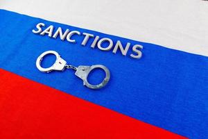 the word sanctions laid with silver metal letters on russian tricolor flag near handcuffs in directly above view photo