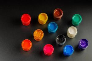 close-up background of opened small gouache paint jars on black surface photo