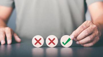 A businessman selects a wooden block with a check mark icon symbol placed on the table,The best alternative decision idea, the solution that has been analyzed and reflected. photo