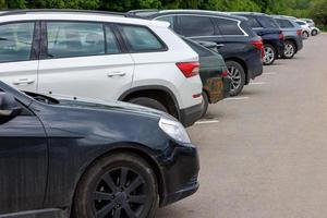 row of different color cars on asphalt parking lot at cloudy summer day photo