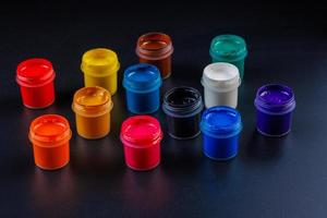 close-up background of opened small gouache paint jars on black surface photo