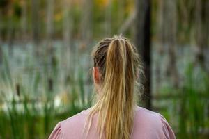 young caucasian woman standing back to camera in evening swamp with blurred dry trees and cattai in the background photo