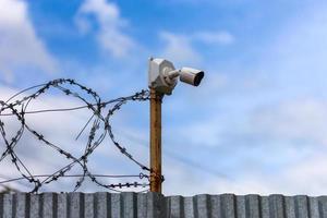 Profiled sheet fence with cheap surveillance camera and barbwire with selective focus. photo