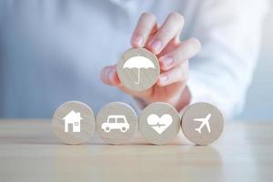 Insurance concept. Protection against a possible eventuality. Hand holding umbrella icon for security symbol and House, Car, Health care and travel icon on wooden circle for assurance life concept. photo