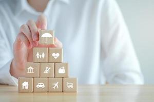 Insurance concept. Protection against a possible eventuality. Hand holding umbrella icon from House, Car, Family, Health, Travel, Business icon on wooden block for assurance life concept. photo