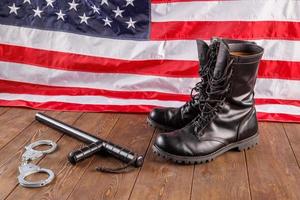silver handcuffs, black boots and police baton near US flag on wooden surface photo