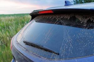 Dirty car glass with wiper and third brake light, rear window covered with a layer of dust. photo