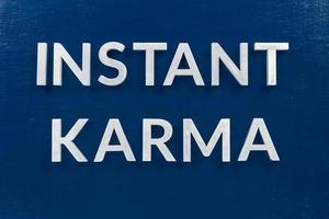 the phrase instant karma laid with silver metal letters on classic blue painted board background photo