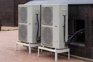 two double condensing units of air conditioner on the ground level near granite building wall photo