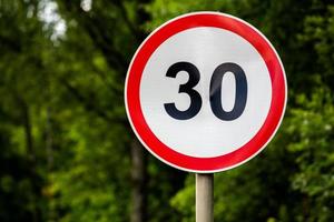 Road sign speed limit 30 kilometers per hour on green forest background with selective focus photo