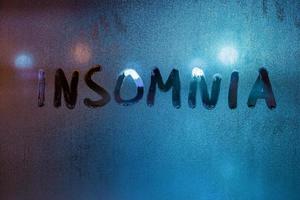 the word insomnia handwritten by finger on night wet window glass close-up with blurred background photo