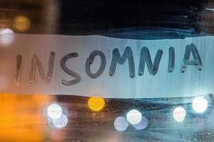 the word insomnia written on night wet window glass close-up with blurred background photo