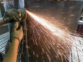 caucasian hands using an angle grinder on metal barrel vessel close-up with long sparks trails photo