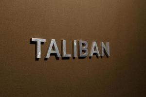 la palabra talibán colocada con letras de metal plateado sobre una tela de lona color caqui marrón áspera foto