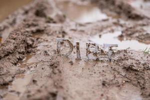 the word dirt composed of silver metal letters on wet clay surface photo