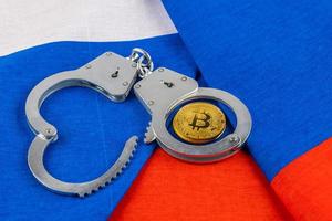 roll of russian paper rubles currency and bitcoin shiner chained with handcuffs on russian flag background photo