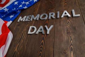 las palabras día conmemorativo colocadas con letras de metal plateado en la superficie de una tabla de madera con una bandera de estados unidos arrugada foto