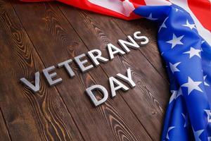 the words veterans day laid with silver metal letters on wooden board surface with crumpled usa flag at right side with diagonal perspective photo
