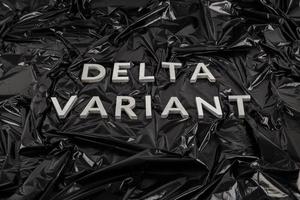 palabras variante delta colocadas con letras de metal plateado sobre fondo de bolsa de plástico negro arrugado foto