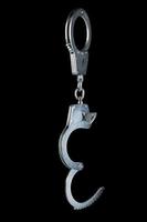 real zinc plated steel police handcuffs half-opened with key hanging vertically, isolated on black background photo