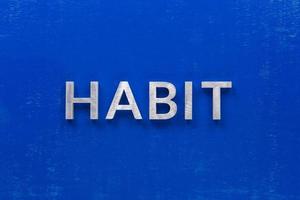 the word habit laid with silver metal characters on blue painted wooden board in central flat lay composition photo